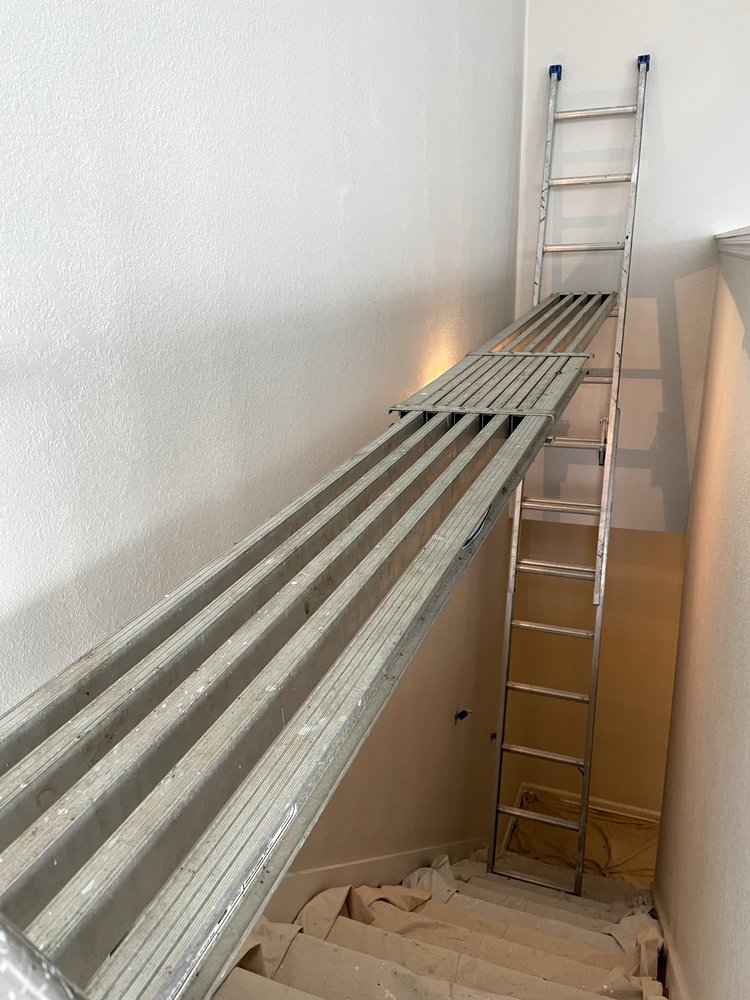 Een afbeelding van een persoon die de muur boven het trapgat schildert met behulp van een ladder, illustrerend het proces van het schilderen boven een trapgat.