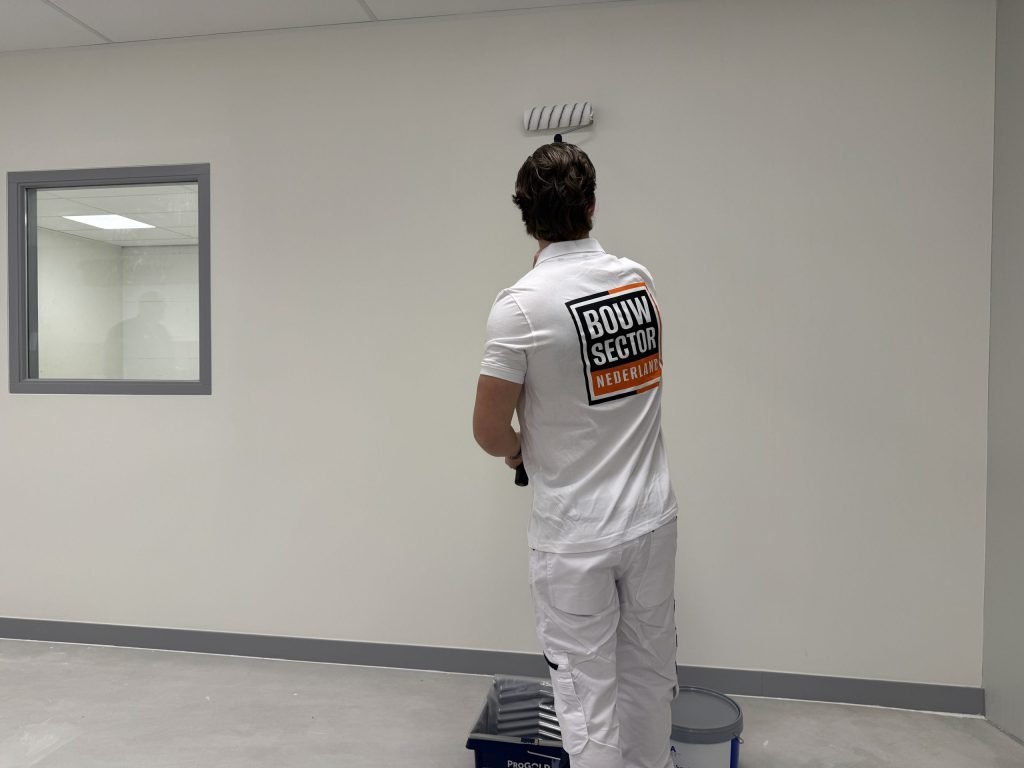 Schilder van Bouwsector Nederland bekijkt een pas gesausde wand in een lege ruimte met een raam