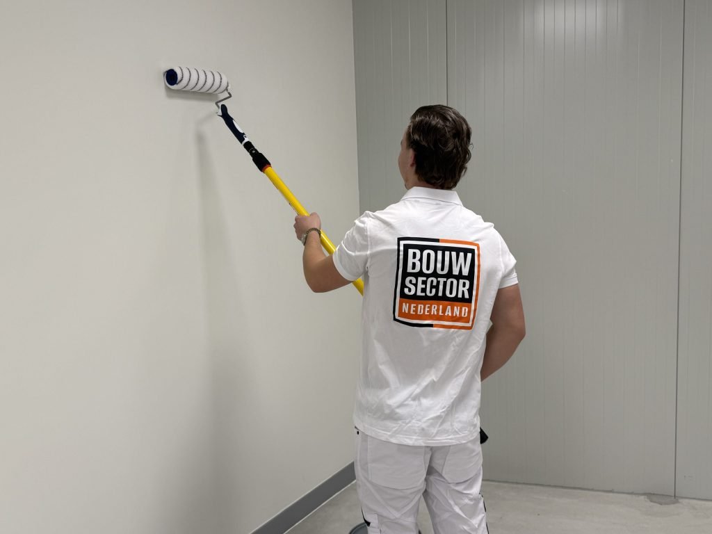 Schilder van Bouwsector Nederland verft de muur met een roller op een verlengsteel