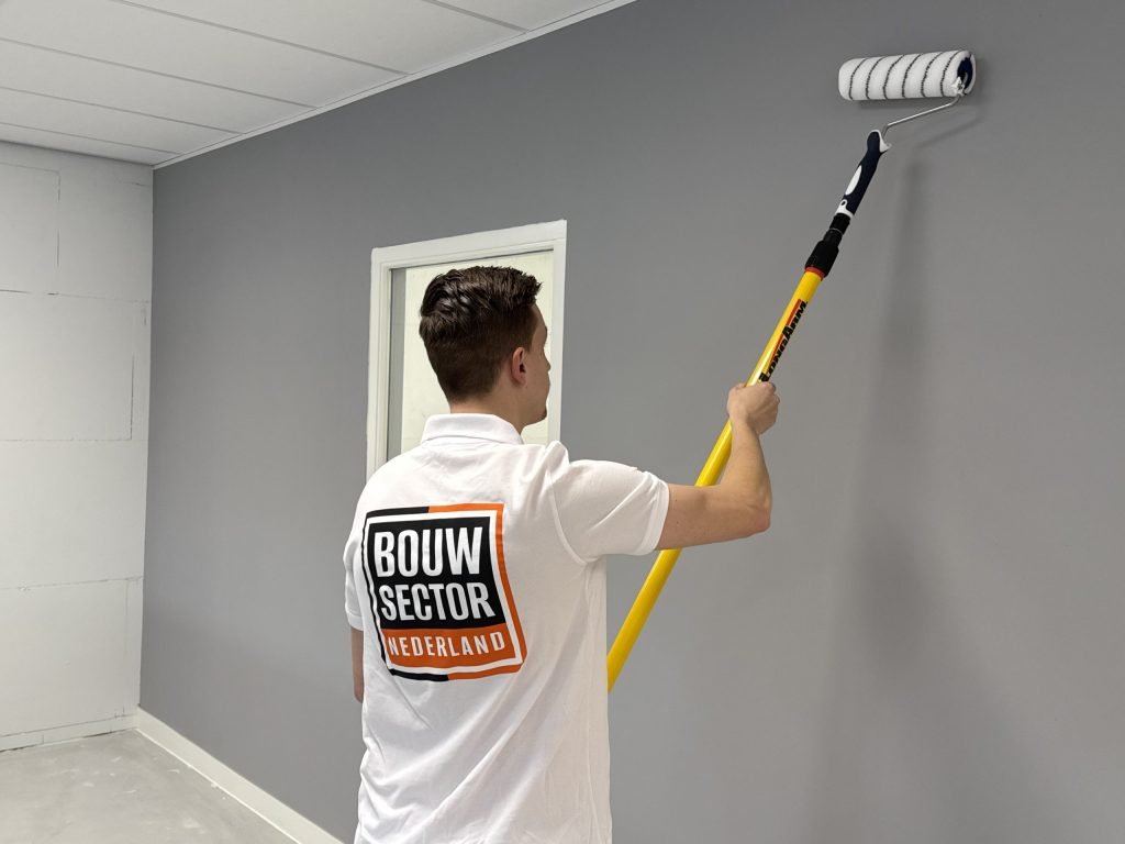 Schilder van Bouwsector Nederland rolt een grijze wand met een roller op een verlengsteel