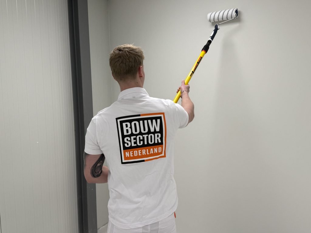 Vakman van Bouwsector Nederland rolt verf op een muur met een roller op een verlengsteel