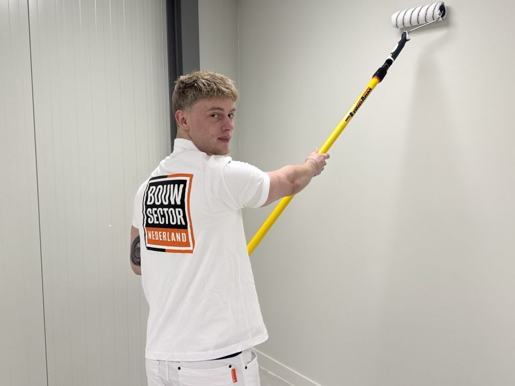 Vakman van Bouwsector Nederland kijkt om terwijl hij een lichte wand rolt met een roller op een verlengsteel